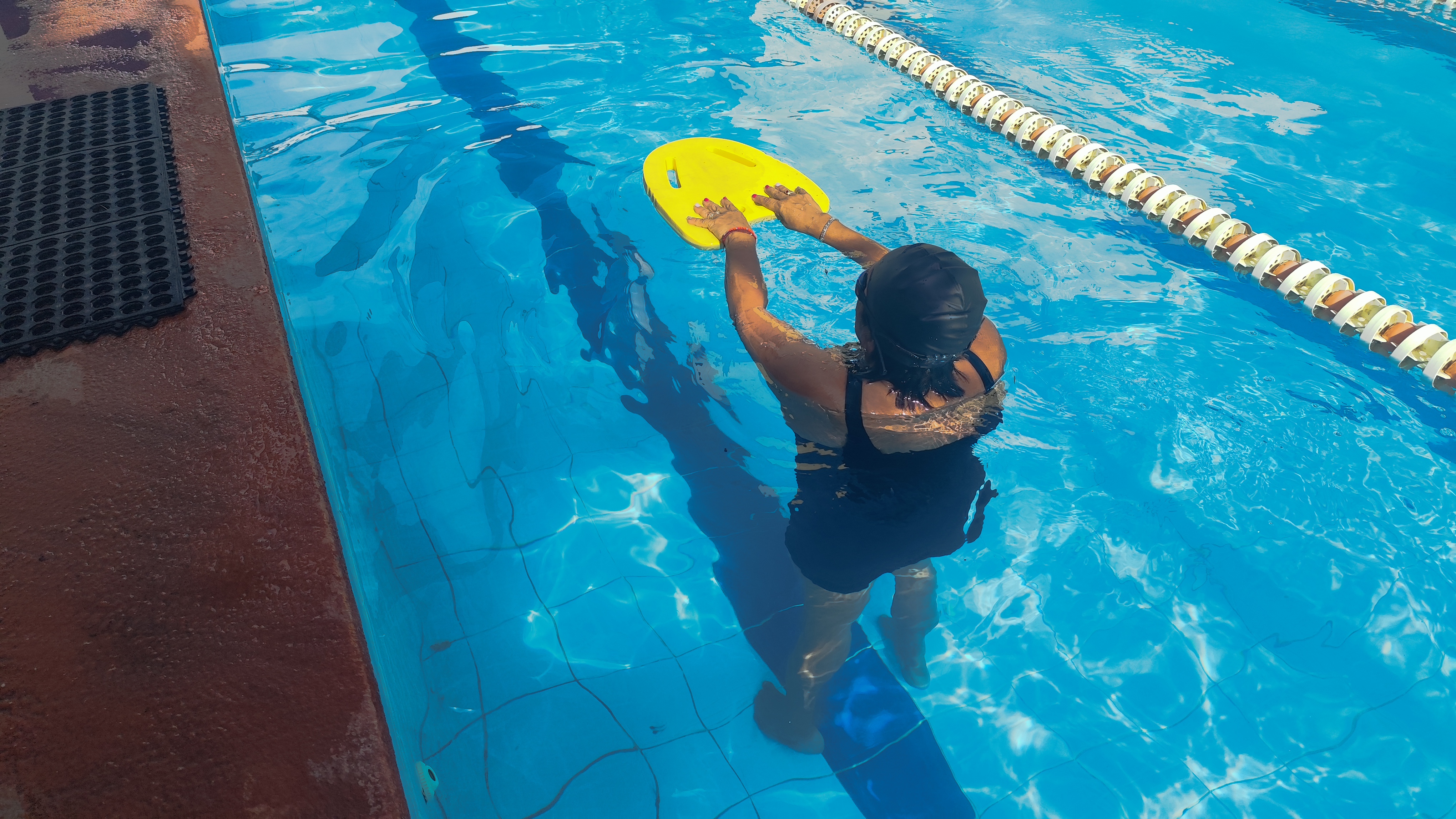 María del Carmen practica en la alberca con una tabla de natación amarilla